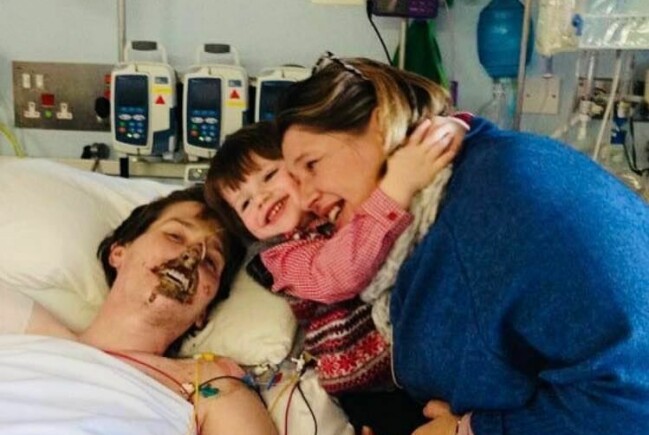 Alex Lewis tillsammans med frun Lucy och sonen Sam. Alex Lewis ligger i en sjukhussäng och bredvid står frun Lucy med sonen Sam i famnen.