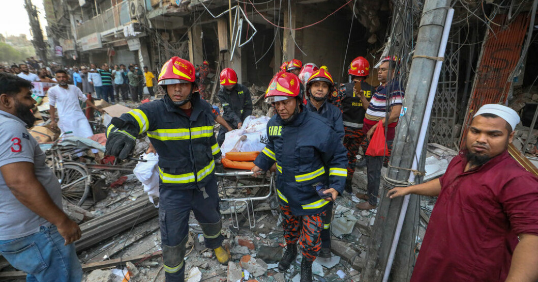 Brandmän bär iväg kvarlevorna av en person som omkom i explosionen. Explosion i kontorshus i Dhaka – tiotal döda
