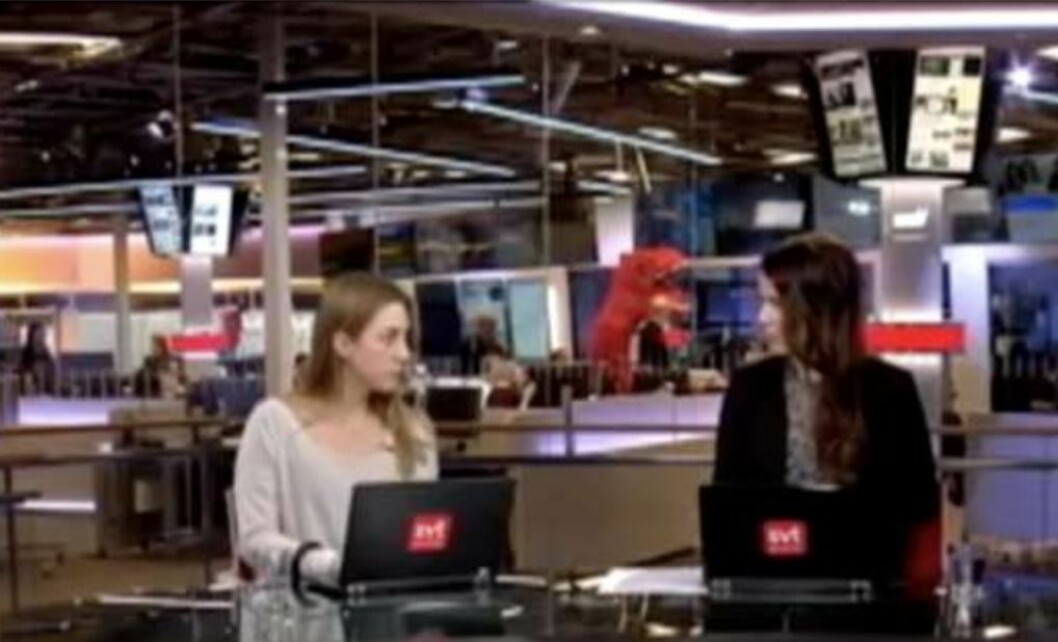 Väder-Nils som röd dinosaurie skymtar i bakgrunden mitt under SVT:s nyhetssändning.