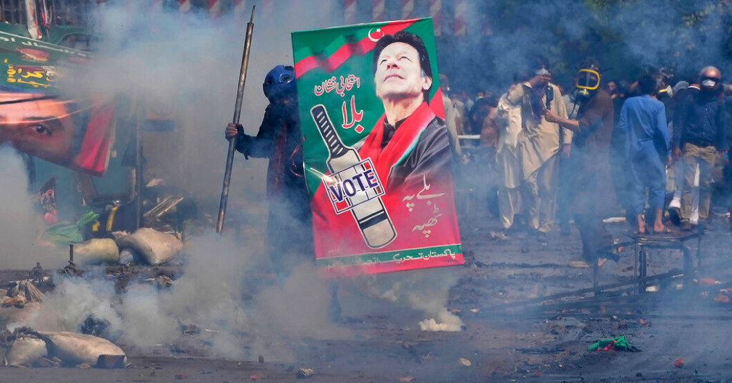 En anhängare till Imran Khan tar skydd bakom ett plakat med dennes bild tidigt på onsdagsmorgonen. Arresteringsorder för Khan dras tillbaka