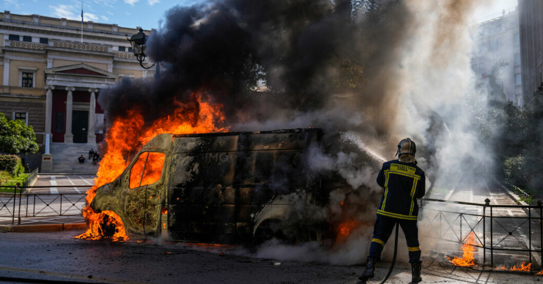 En brinnande bil i centrala Aten under onsdagens transportstrejk som äger rum runtom i Grekland. Tiotusentals greker i protest efter tågolycka