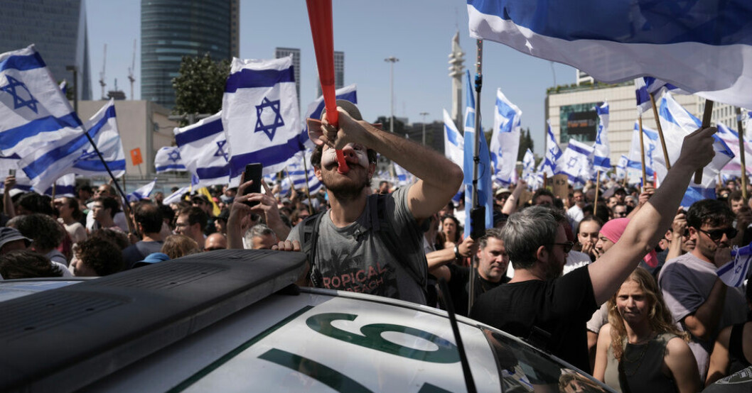 En demonstrant i grismask blåser i en vuvuzela bredvid en polisbil i Tel Aviv. Våldsamma protester mot israelisk rättsreform
