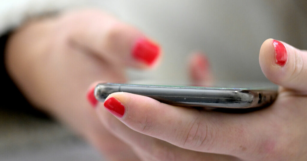 En person med nagellack håller i en mobiltelefon.