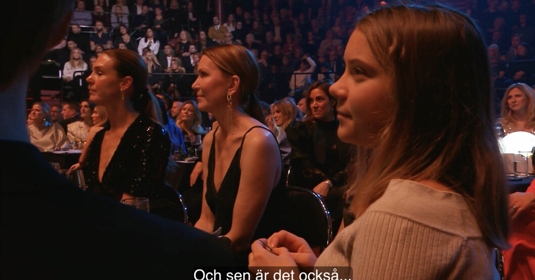 Greta Thunberg syns sitta och virka samtidigt som hon följer prisutdelningen på scenen.