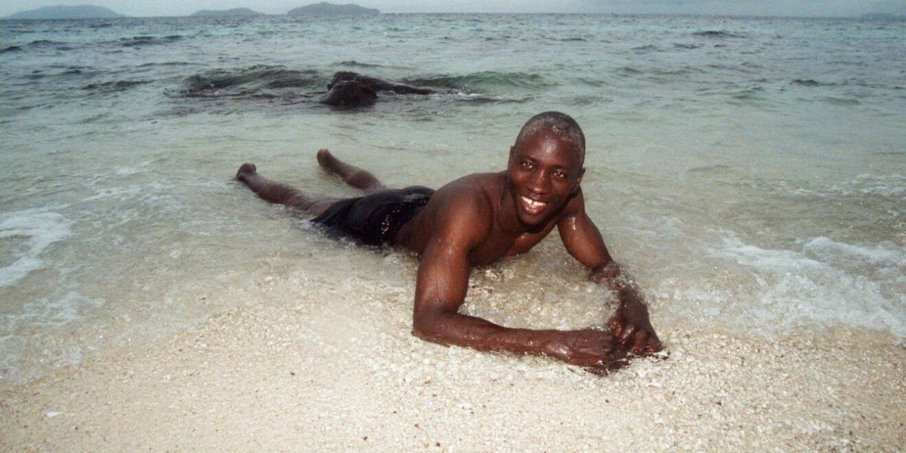 Buba Badjie i Robinson 2000, i svarta badbyxor på en strand.