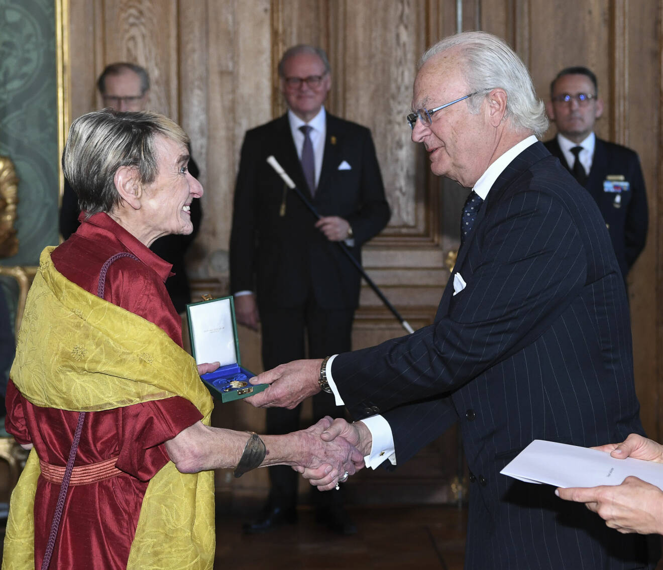 Gunilla Bergström tar emot en kunglig medalj av kung Carl XVI Gustaf.