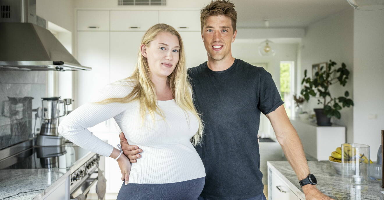 Calle Halfvarsson håller om gravida sambon Isabell Olsson hemma i deras kök.