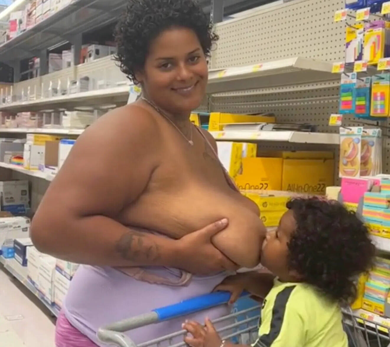 Mamman håller i sitt bröst och låter barnet som sitter i kundvagnen äta.