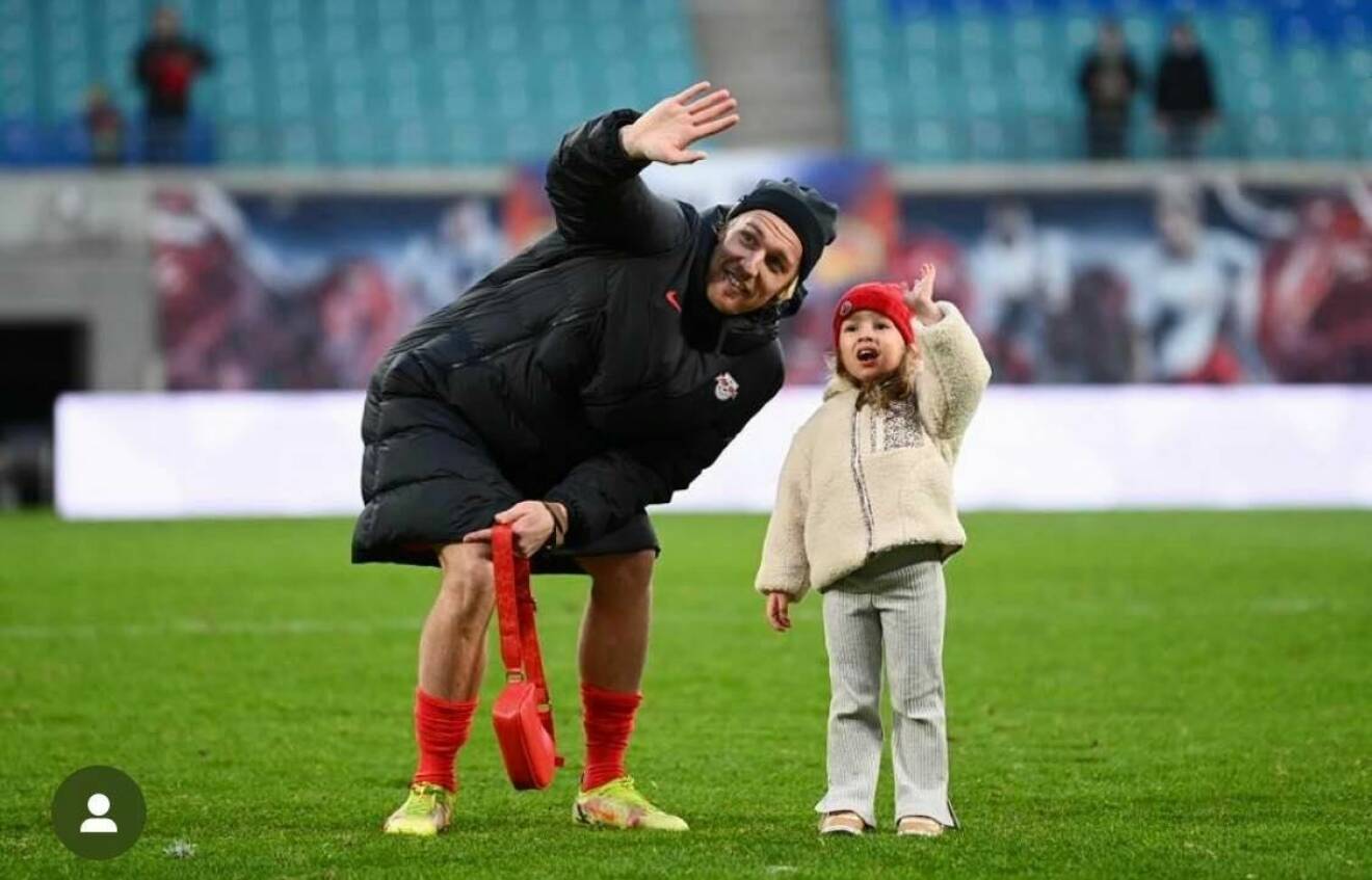 Emil Forsberg vinkar på en fotbollsplan tillsammans med dottern Florence
