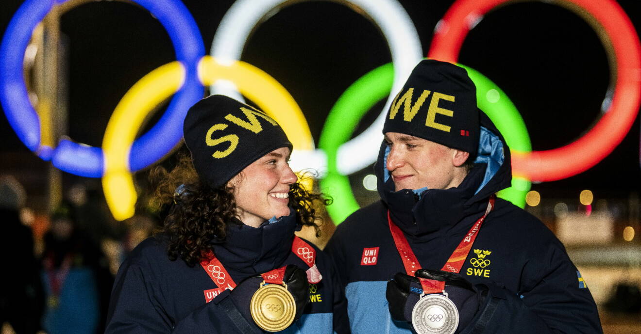 Hanna Öberg och Martin Ponsiluoma håller upp sina OS-medaljer under vinter-OS i Peking 2022 och tittar på varandra.