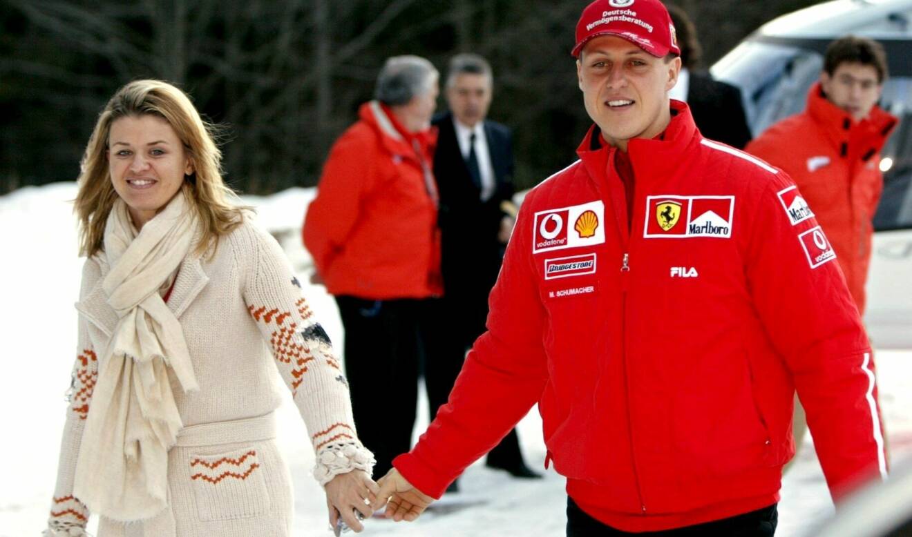 Corinna och Michael Schumacher håller handen och ler medan de går.