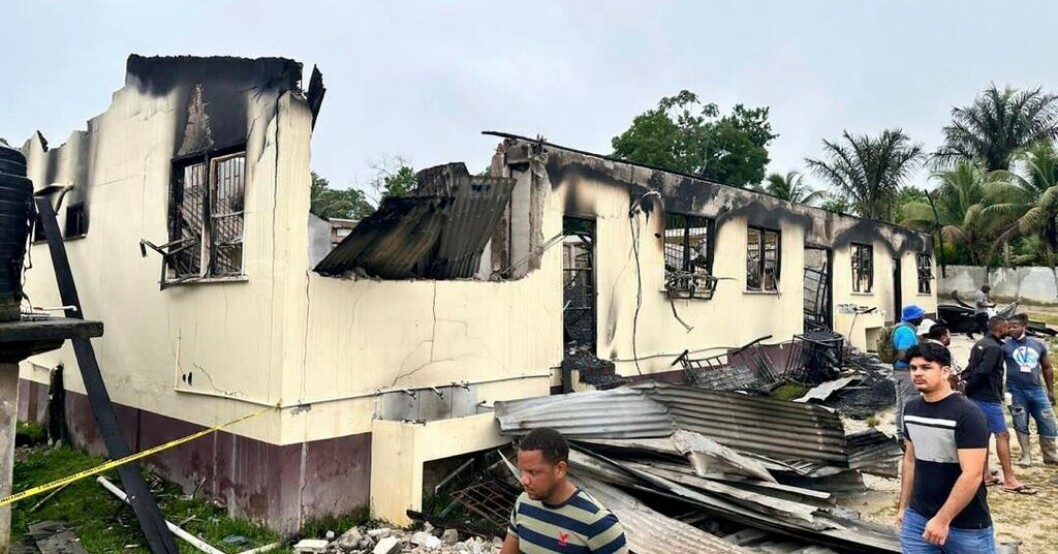 Invånare utanför resterna av den brandskadade sovsalen i Guyana. Många barn döda i brand i Guyana