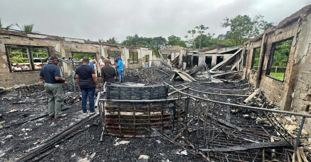 Invånare utanför resterna av den brandskadade sovsalen i Guyana. Elev misstänks ligga bakom dödliga branden