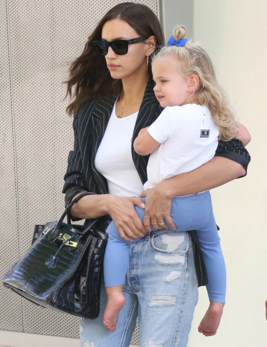 Irina Shayk har numera hand om dottern varannan vecka. Irina Shayk har jeans, vit t-shirt och svart kavaj och bär sin dotter på höften