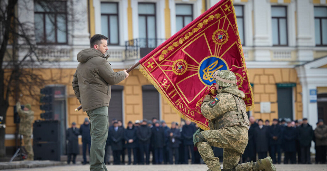 President Zelenskyj håller upp en militär flagga som en officer får kyssa, under fredagens årsdagsceremonier i Kiev. Segerviss Zelenskyj: Sanningen är på vår sida