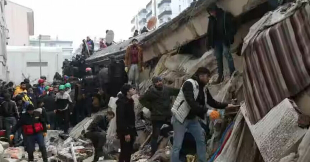 Människor framför en rasad byggnad i Antakya i Turkiet.