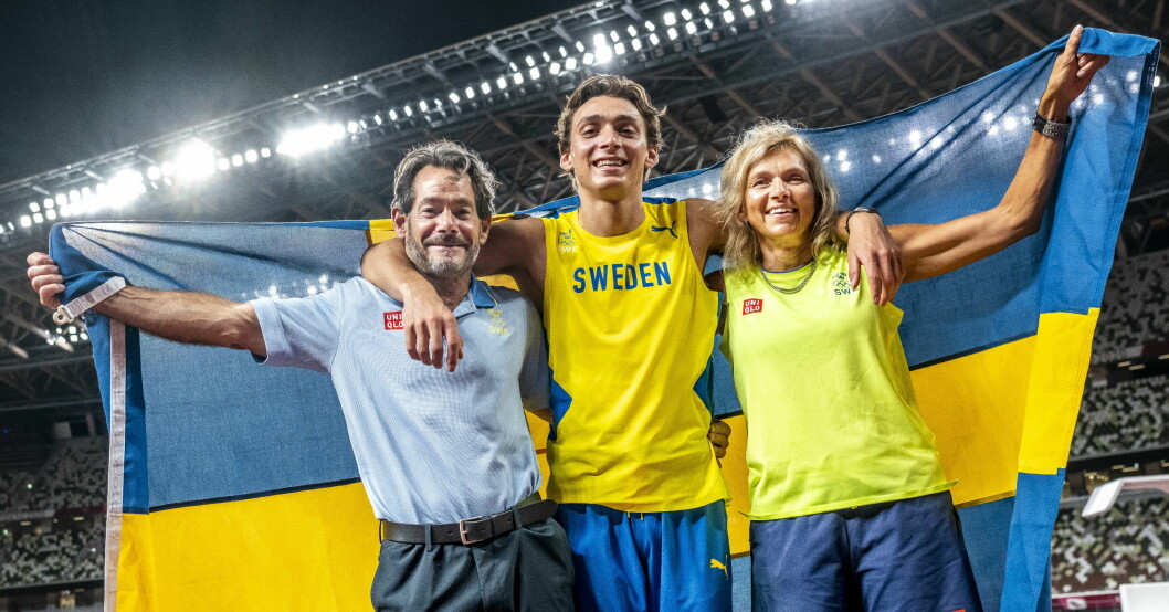Armand Duplantis med sina föräldrar efter att ha vunnit OS-guld ii stavhopp i Tokyo 2021. Greg, Armand och Helena Duplantis håller upp en flagga bakom sig.