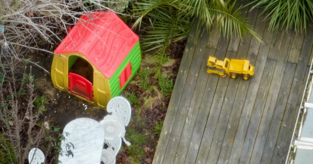 Barnens leksaker ligger kvar på baksidan av radhuset. En grävmaskin på terassen och ett färgglatt tält i hårdplats på en bakgård.