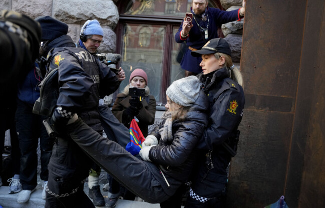 Två norska poliser bär Greta Thunberg i både armar och ben för att ta bort henne från departementens ingångar. Två norska poliser bär Greta Thunberg i både armar och ben för att ta bort henne från departementens ingångar.