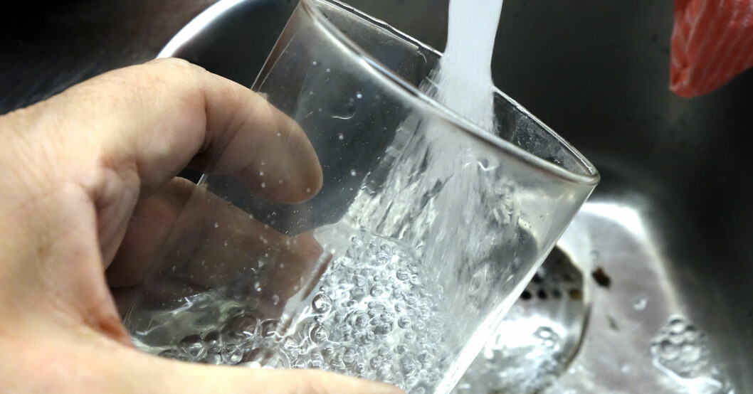 En hand håller i ett vattenglas som fylls med vatten i en diskho.