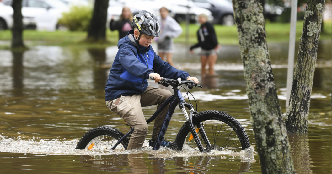 En pojke cyklar genom vattenmassorna efter nattens kraftiga skyfall. Cykla på vattnet