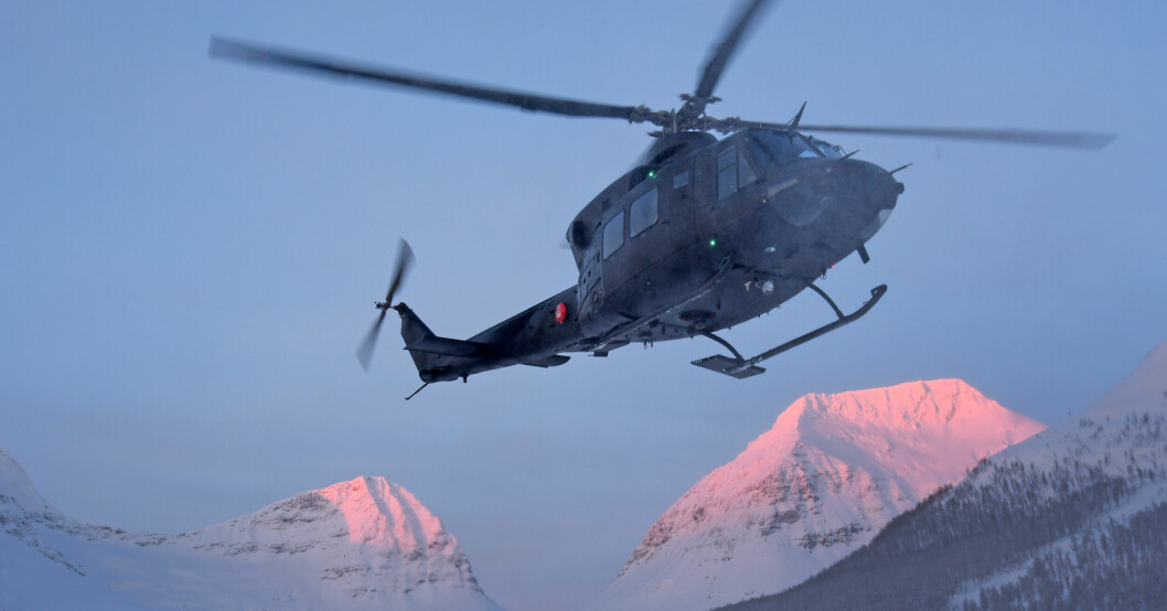 En räddningshelikopter flyger med snötäckta fjäll i bakgrunden.