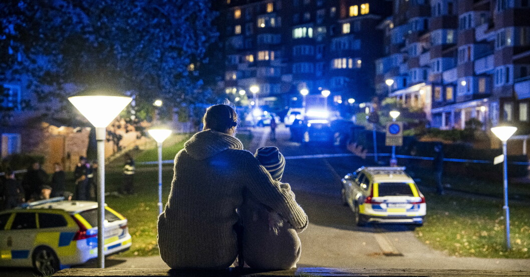 En mamma håller om sitt barn med en stor polisavspärrning framför och flera polisbilar.