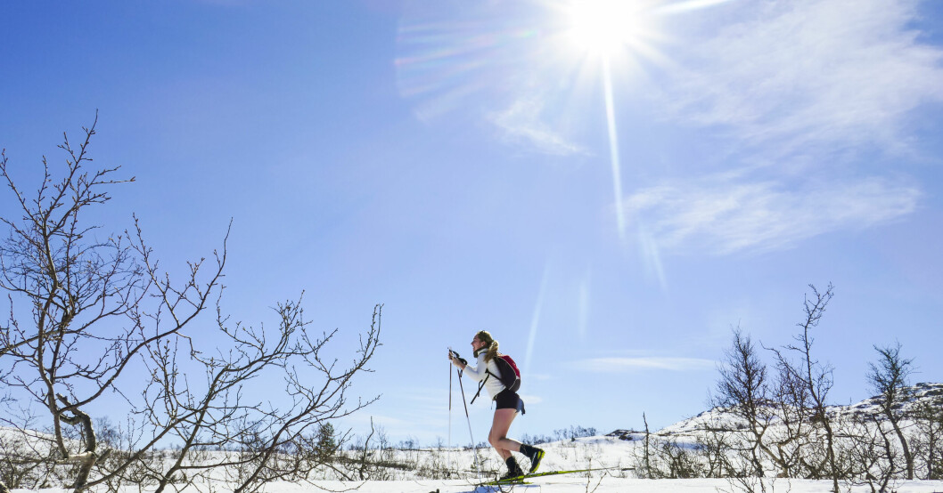 En kvinna åker skidor i shorts i strålande solsken.