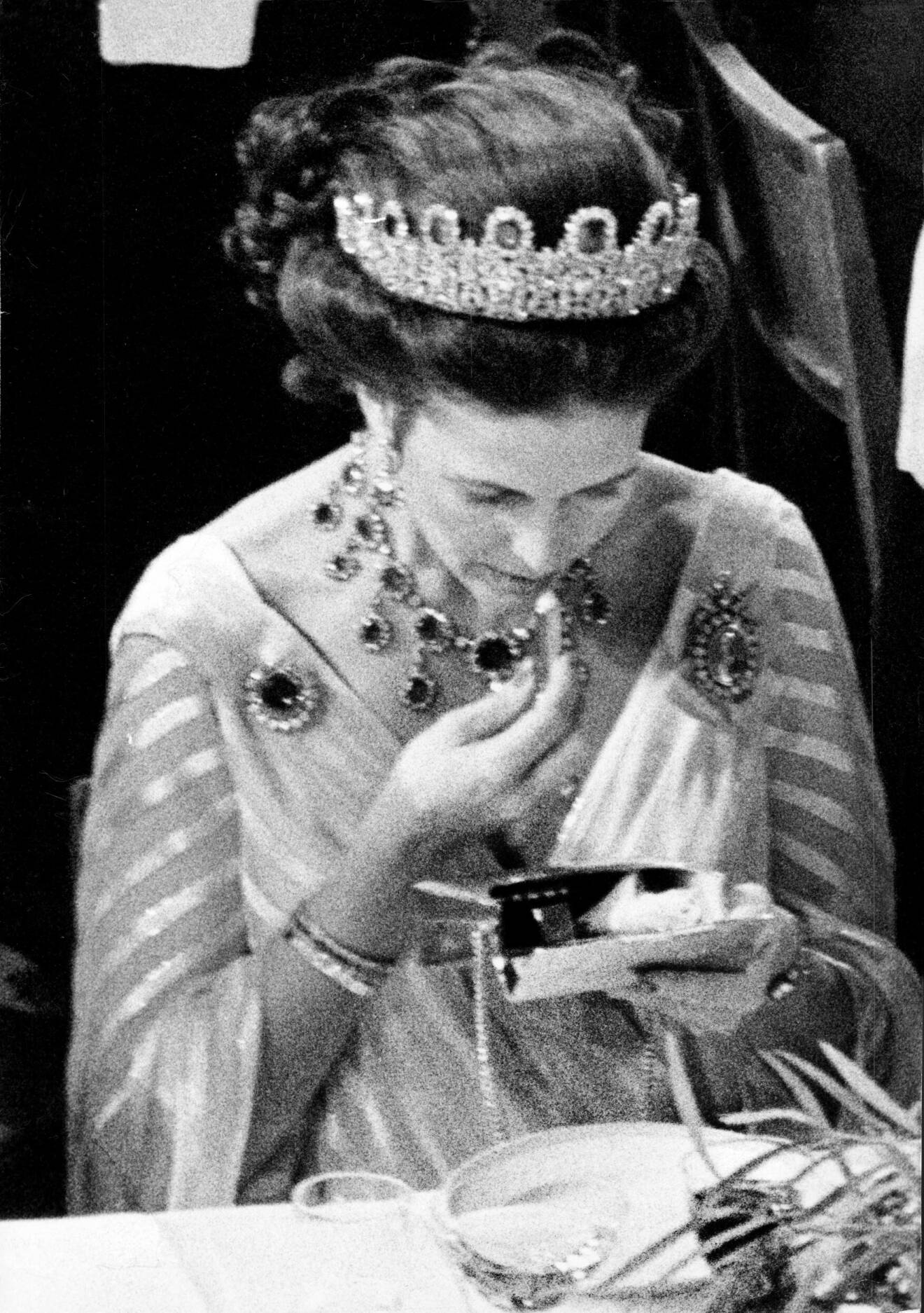 Silvia, drottning Sverige. Nobelfesten 1981. Drottningen smyger upp ett läppstift och en sminkspegel och bättrar på sminket, ett etikettsbrott under middagen